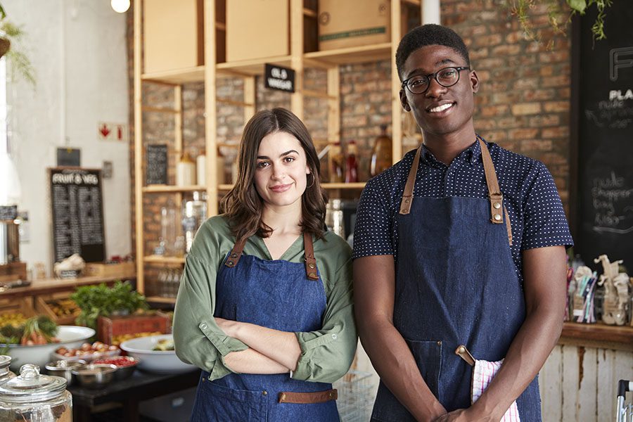 Business Insurance - Male and Female Wearing Blue Aprons Stand Together inside Their Grocery Store